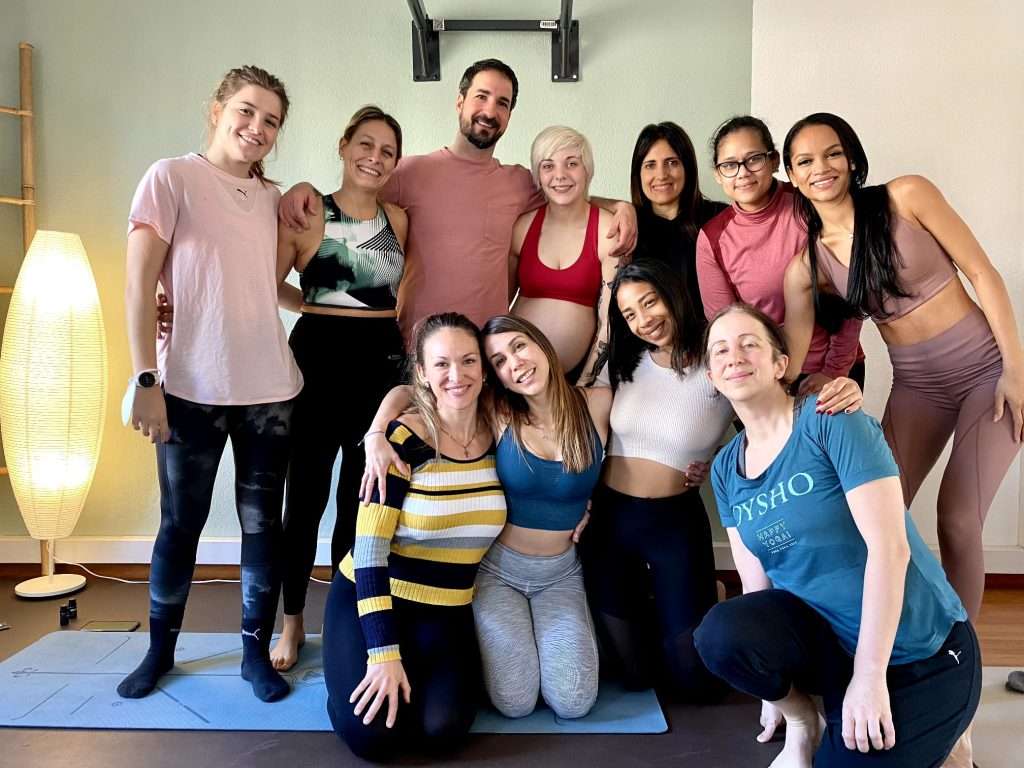 Grupo de 11 personas sobre un mat de yoga sonrientes después de una clase de yoga